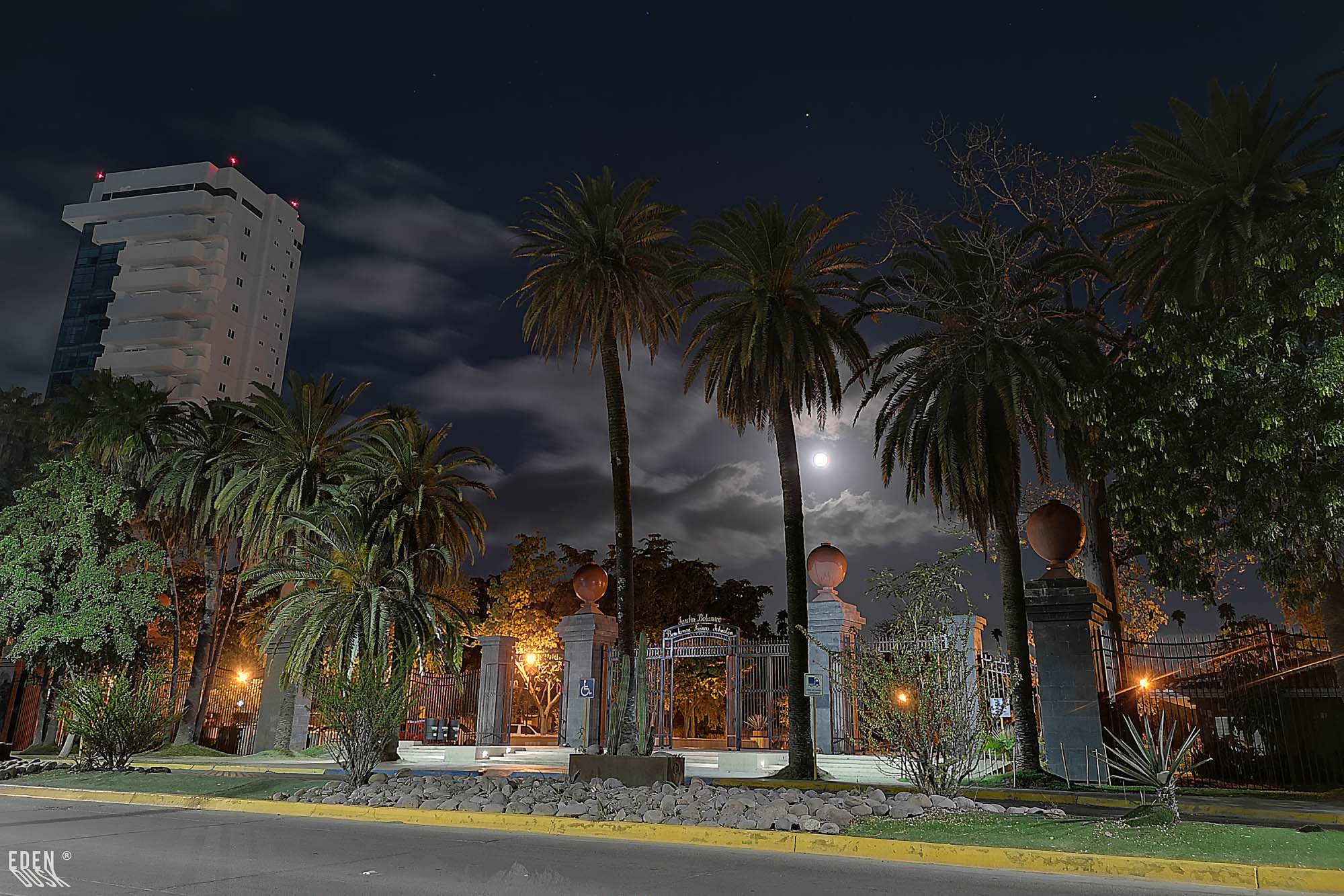 Las altas palmeras enmarcan el portón de entrada del Parque Sinaloa, ambos elementos iluminados bajo el cielo nocturno.