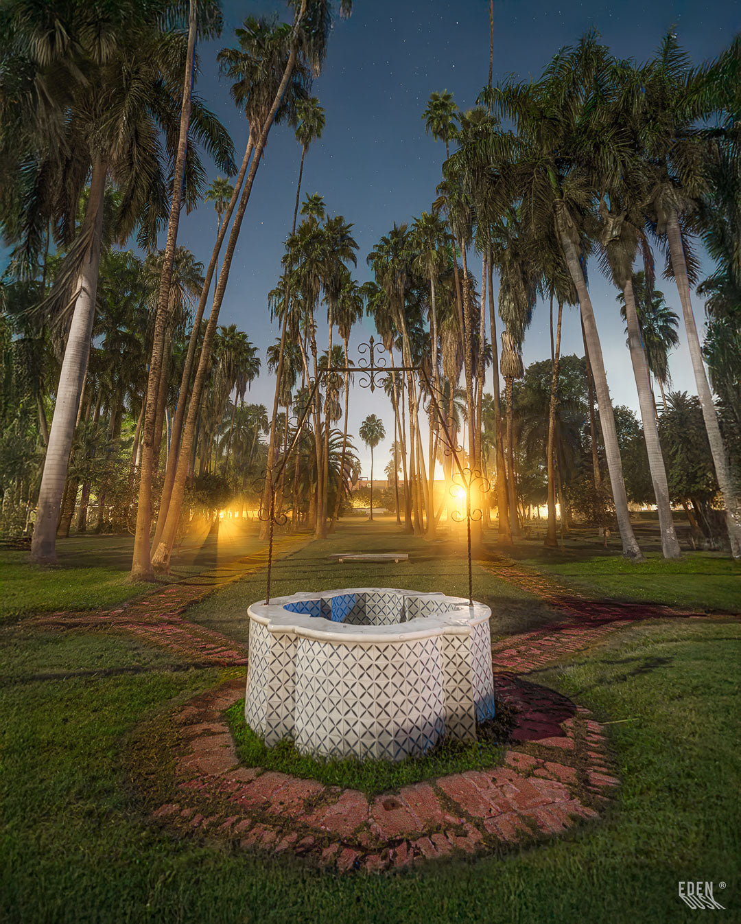 El pozo de piedra del Parque Sinaloa se erige como un centinela nocturno, bajo la mirada de altas palmeras iluminadas.