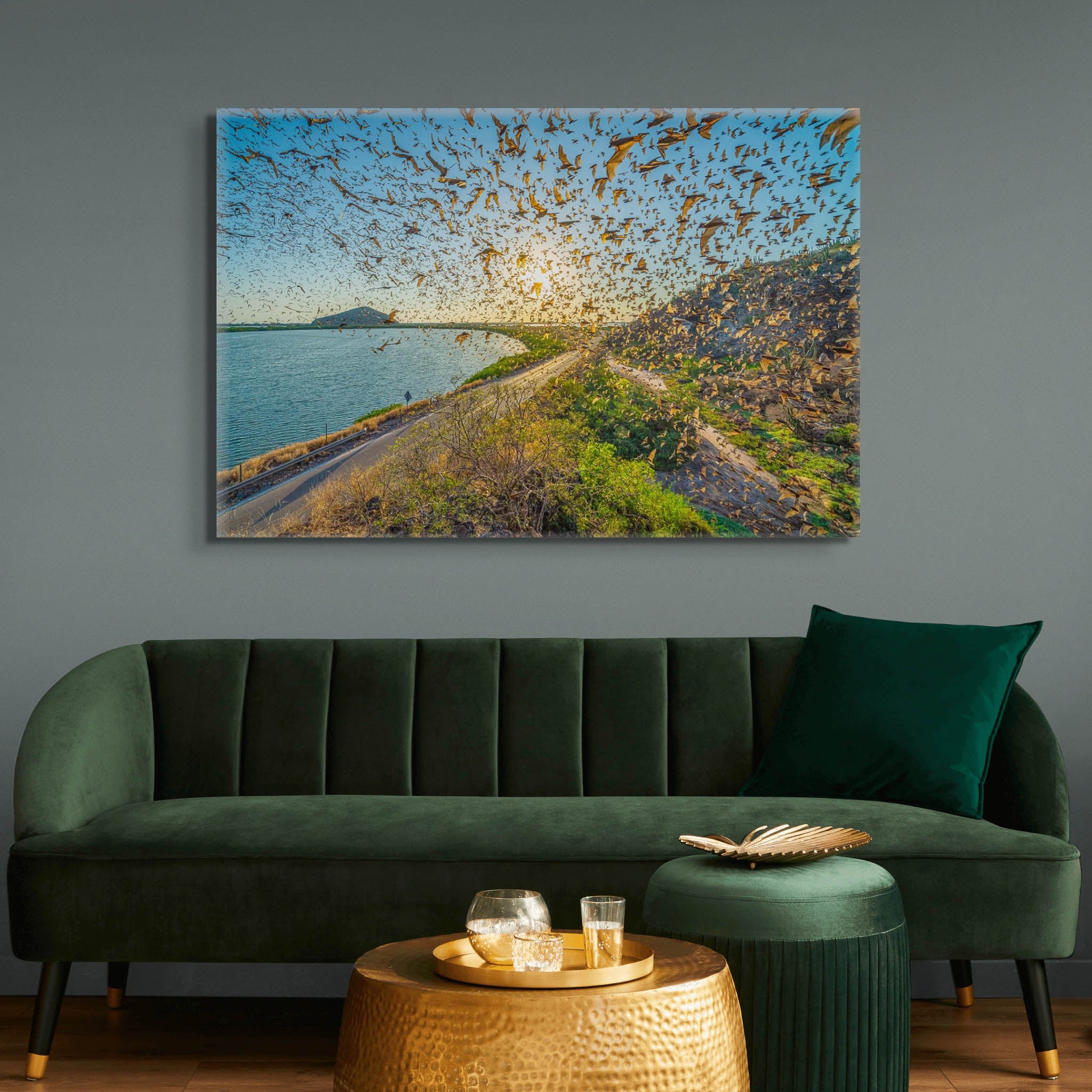 Canvas en sala sobria; miles de murciélagos cruzan el cielo al atardecer sobre camino costero y cuerpo de agua; luz dorada y movimiento dinámico.