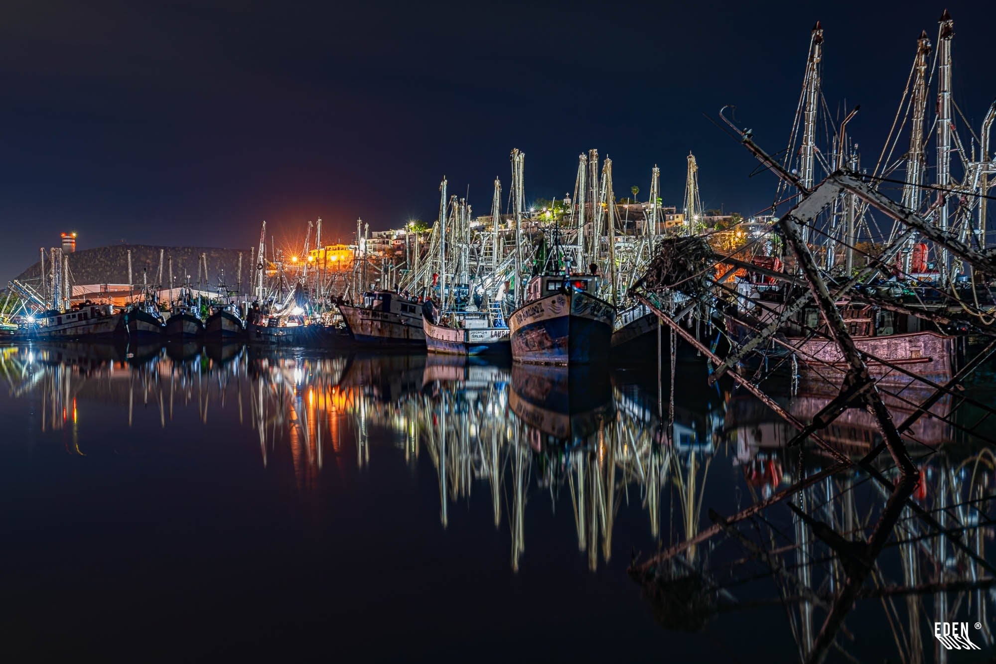 Flota camaronera en el muelle de Topolobampo durante la noche, mástiles y luces reflejadas en el agua en calma, Sinaloa.