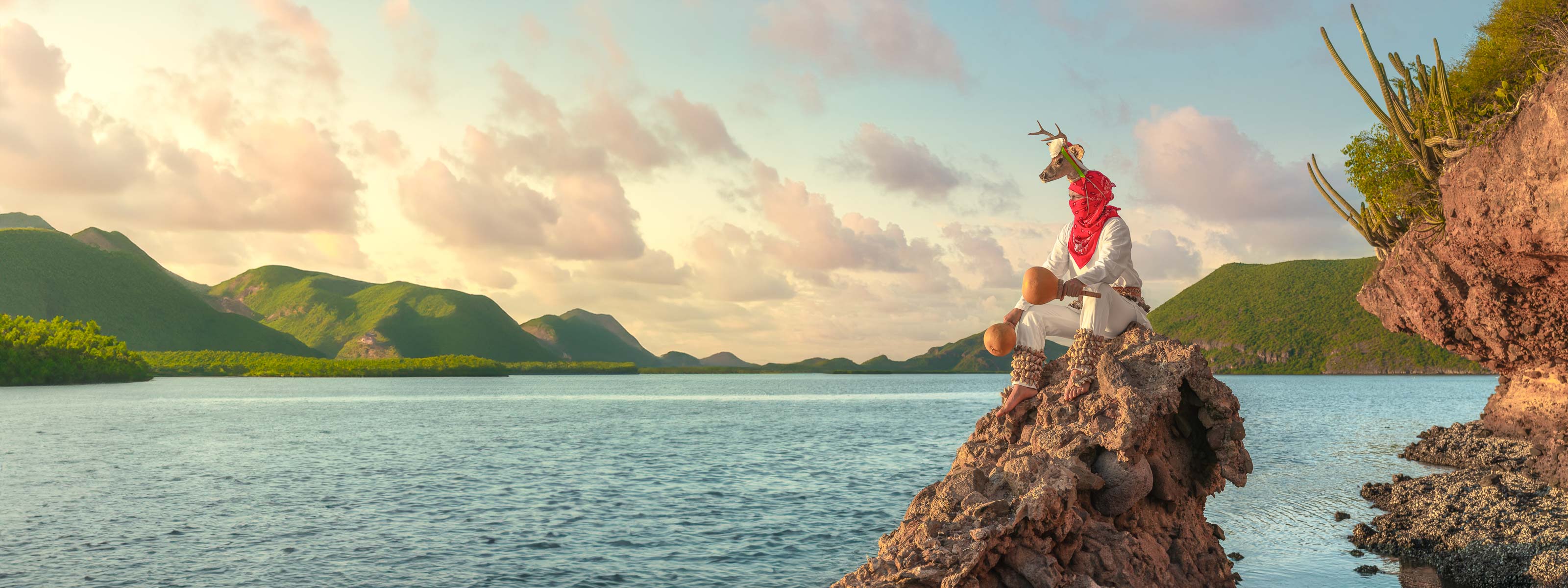 Danzante de venado yoreme sobre roca, gesto sereno y luz cálida del atardecer; mar al fondo difuso, encuadre horizontal