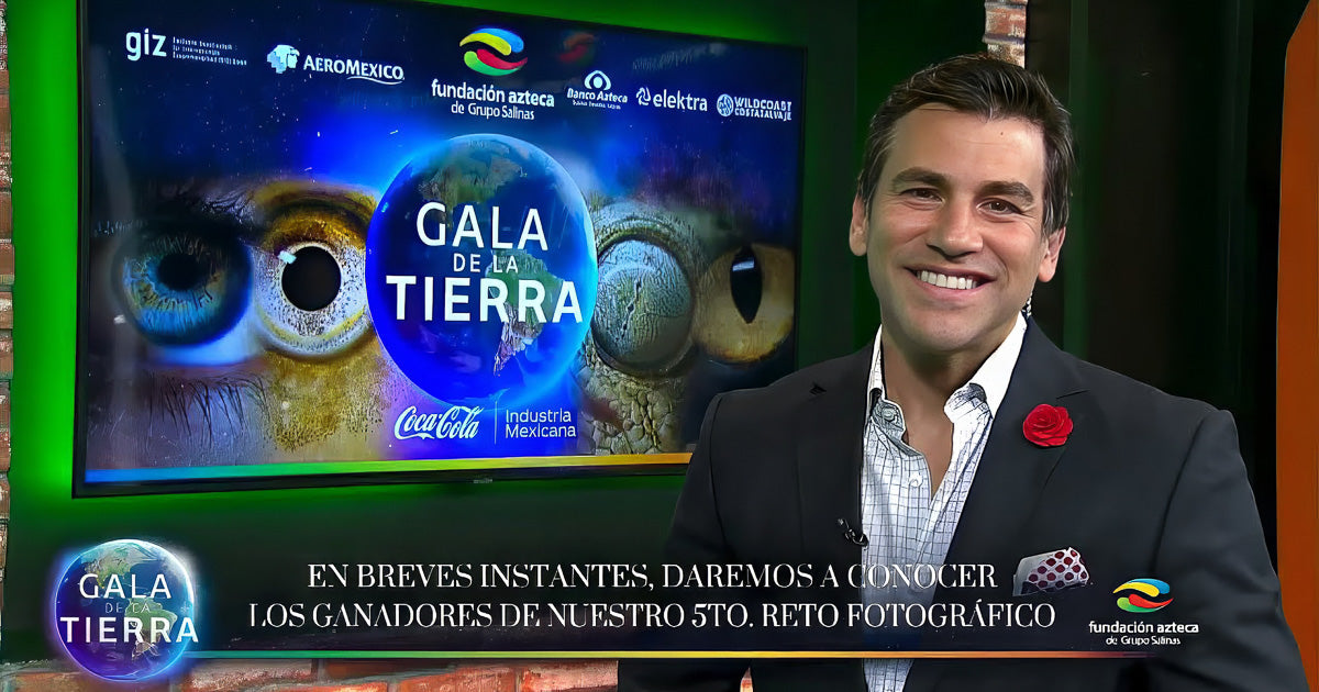 Presentador sonriente en set de televisión junto a pantalla con el logotipo Gala de la Tierra y marcas aliadas; encuadre medio y luz de estudio.