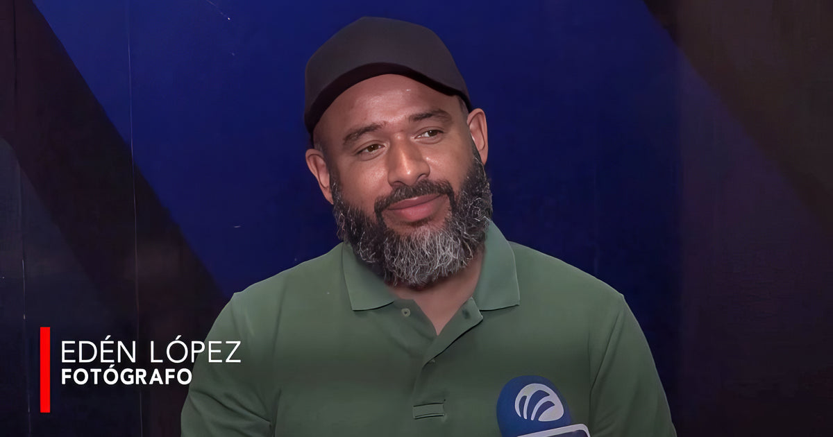 Primer plano de Edén López, fotógrafo, durante una entrevista en televisión; lleva gorra negra y polo verde, con un micrófono al frente y fondo azul oscuro.