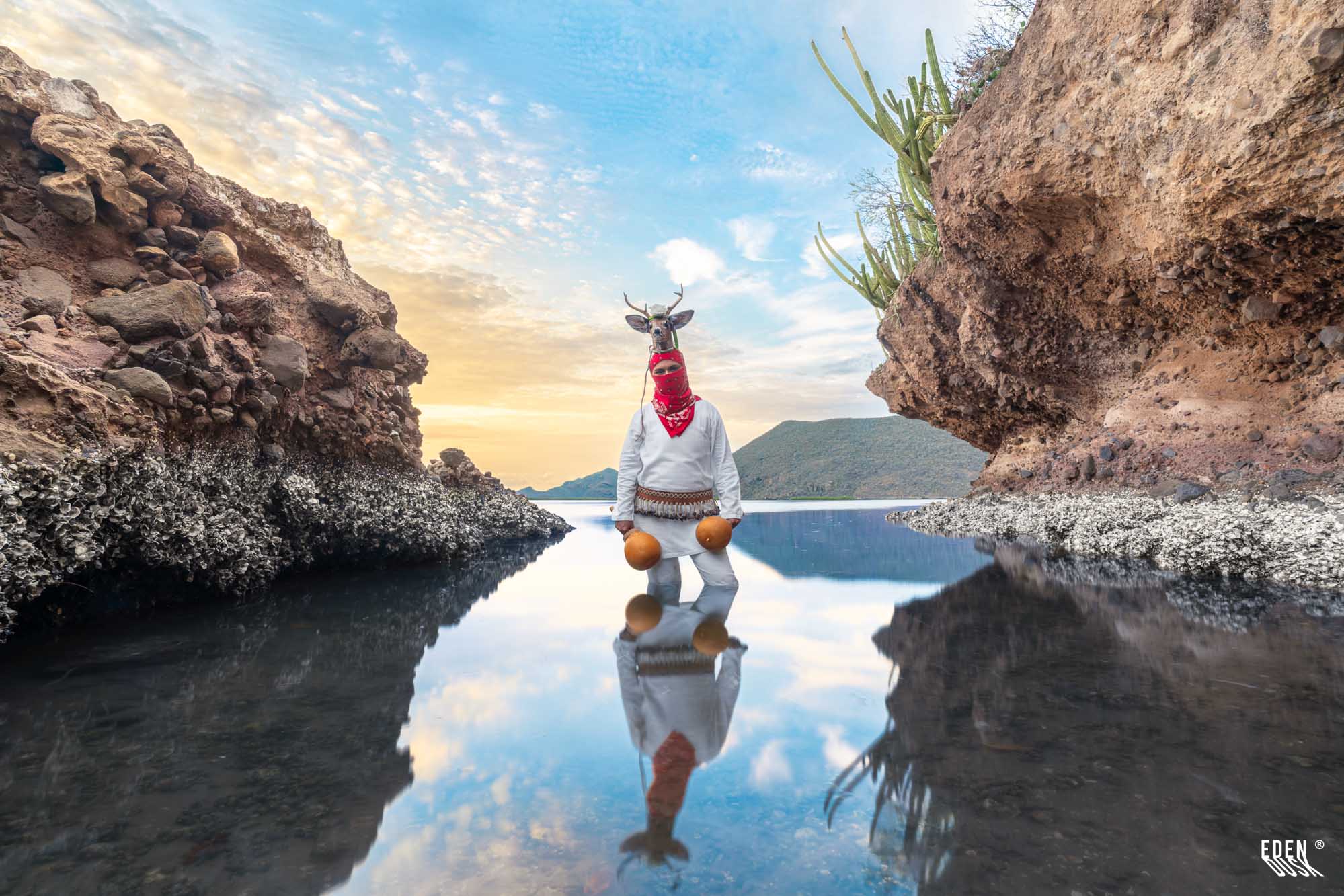 Figura del Venado en canal entre rocas; reflejo en agua calma, cielo claro.