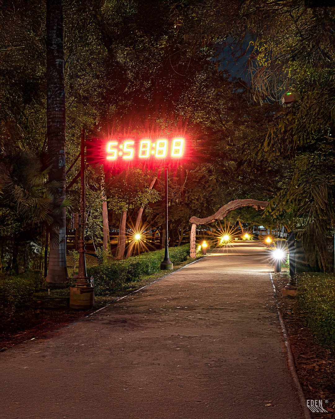 El emblemático cronómetro del Parque Sinaloa se destaca en una escena nocturna, junto a un sendero que se pierde en la distancia iluminado por faroles.