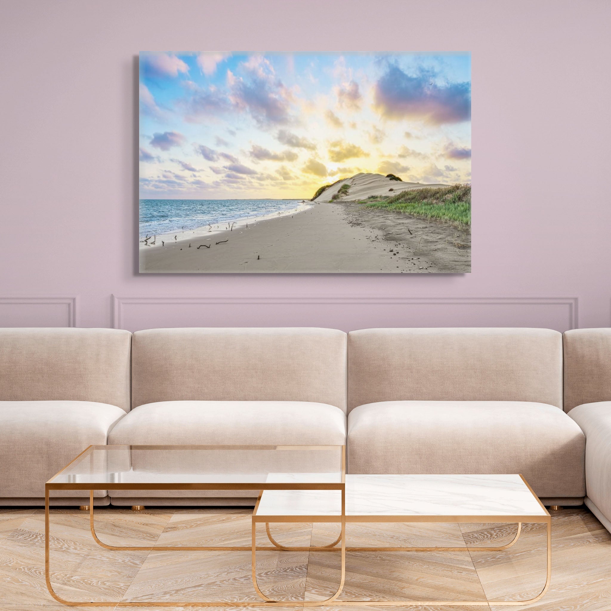 Fotografía de duna costera bañada por luz dorada al amanecer; mar en calma a la izquierda y cielo azul con nubes suaves sobre arena y vegetación.