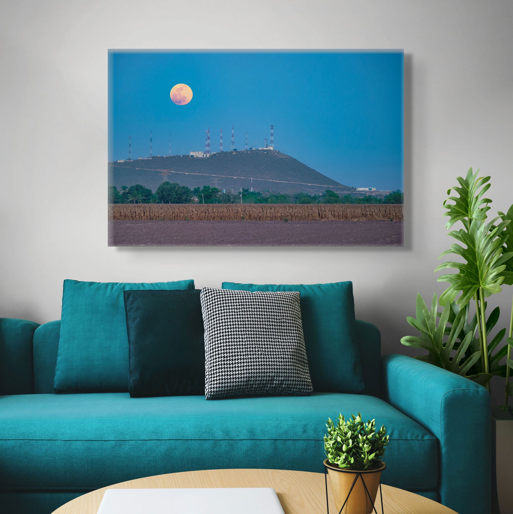 Canvas en interior neutro; luna llena de tono cálido ascendiendo en cielo azul, silueta baja de colina con antenas y franja agrícola en primer plano; atmósfera serena.