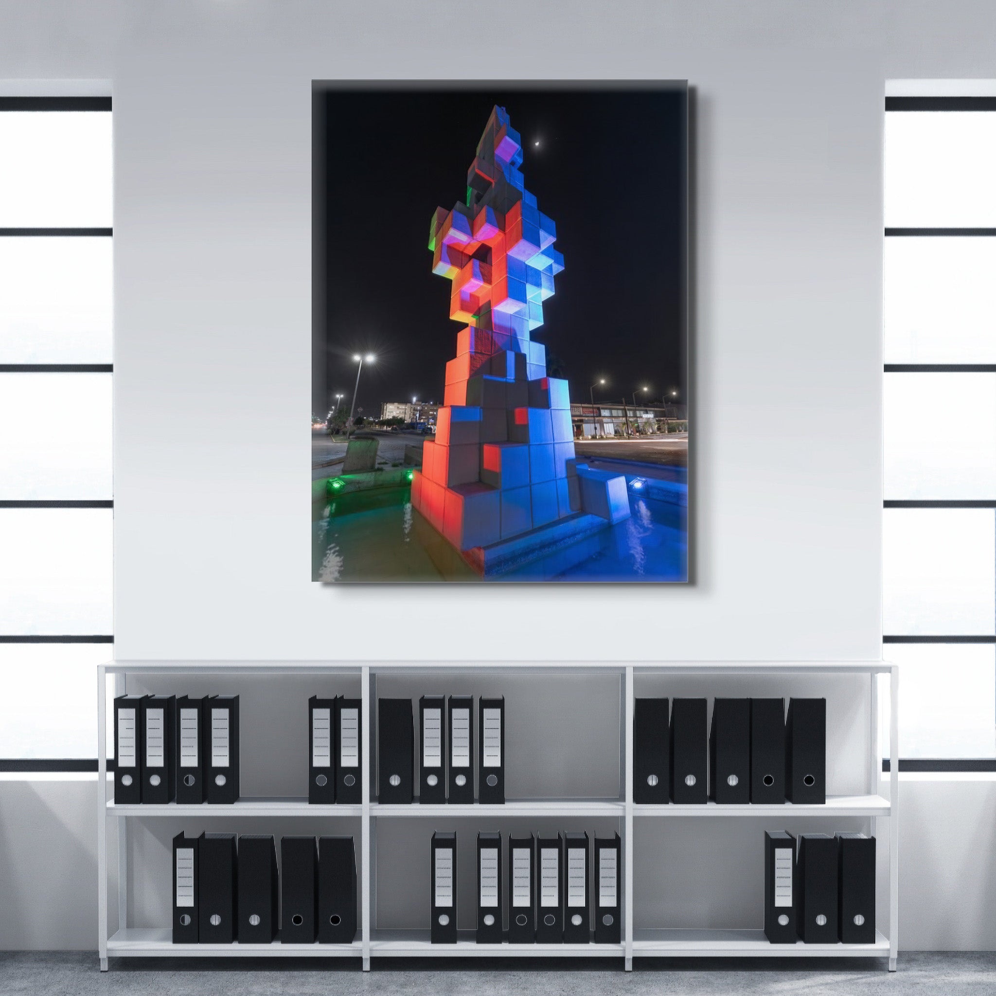 Canvas en interior sobrio; escultura de cubos iluminada en tonos rojo y azul junto a espejo de agua; atmósfera nocturna equilibrada y serena.